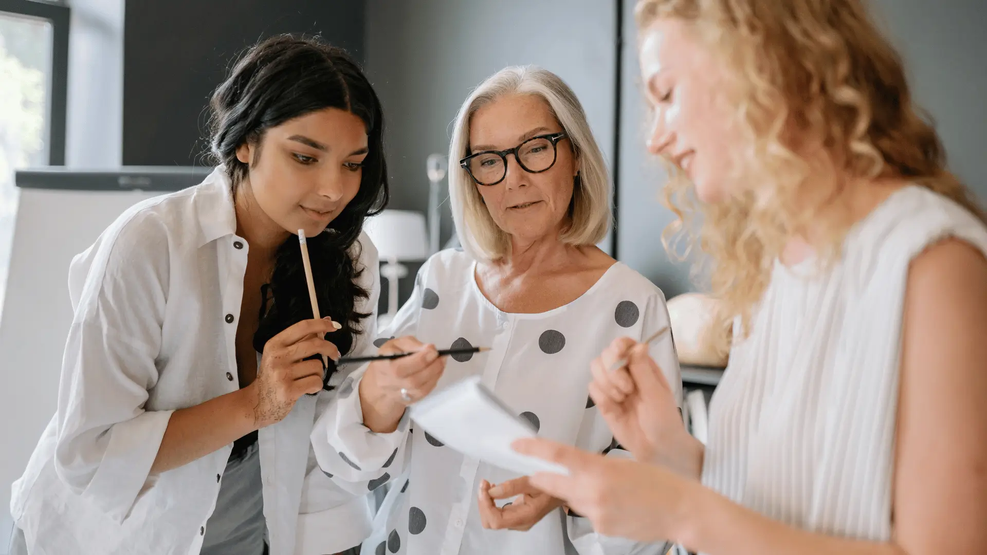 Three professional women collaborating over documents in bright office setting