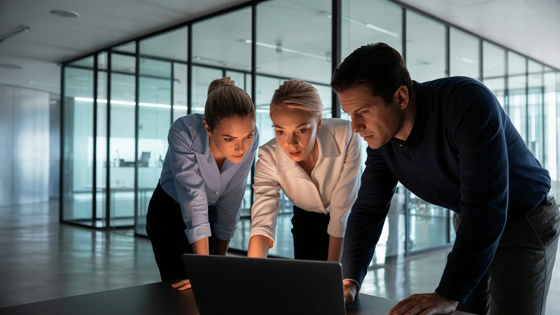 Three focused professionals reviewing strategy together in glass-walled executive office