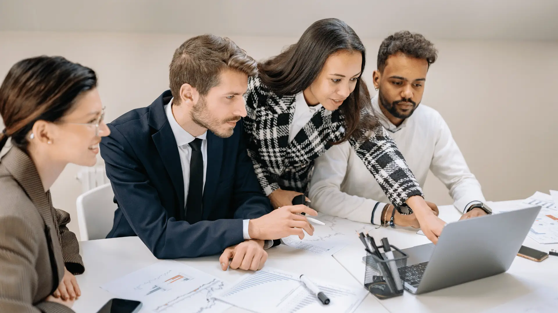 Four financial professionals reviewing planning documents and laptop at white conference table