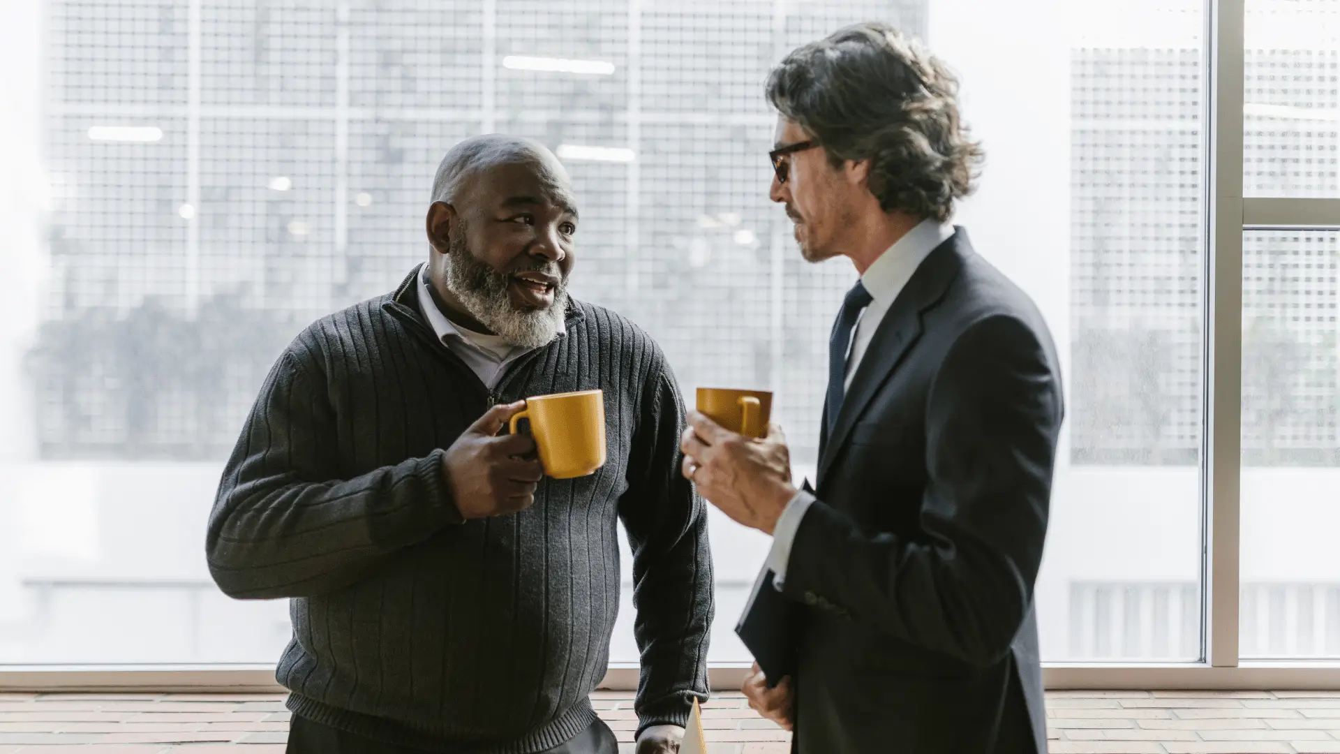Two senior financial professionals sharing ideas over coffee near office window