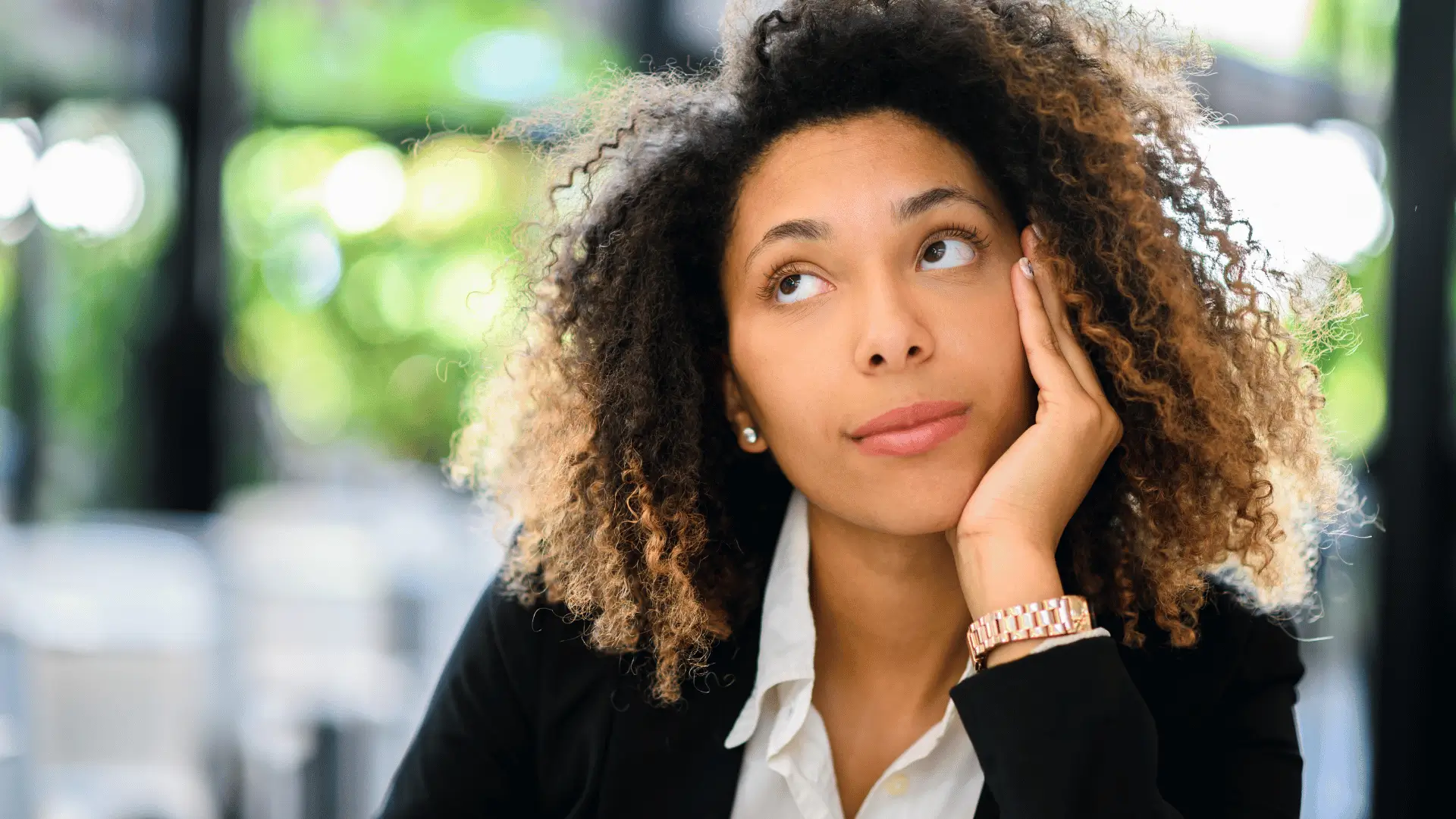Black professional woman in blazer looking upward thoughtfully in outdoor setting