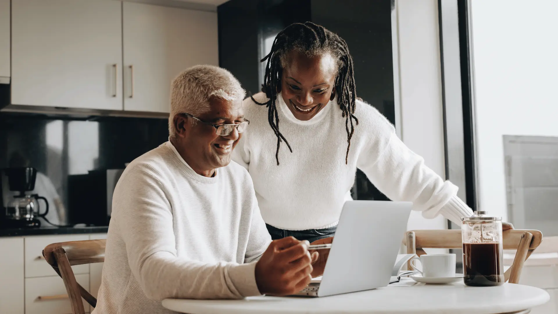 Retired couple smiling while reviewing retirement planning on laptop at home