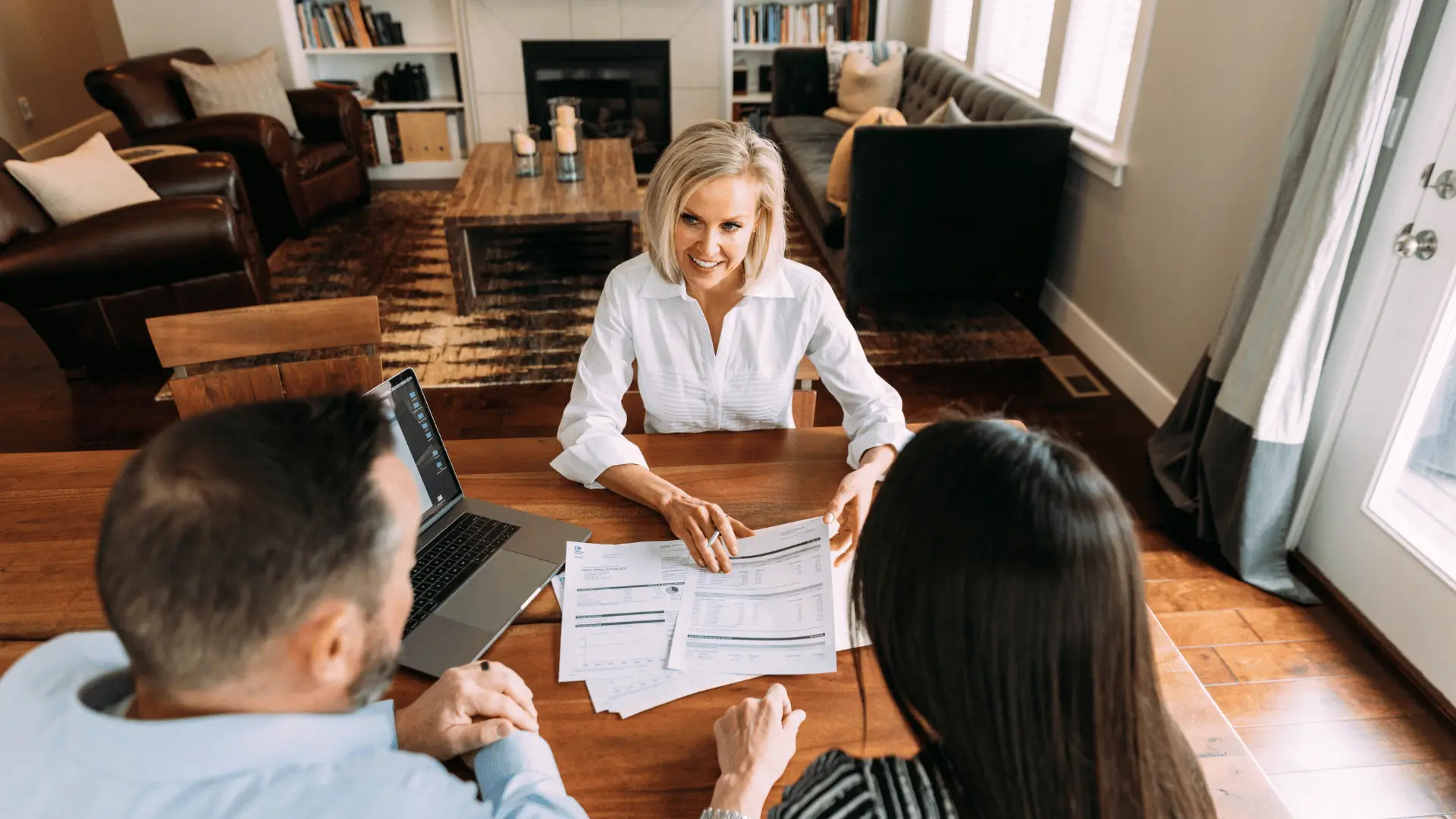 Female financial advisor reviewing planning documents with client couple at wooden table