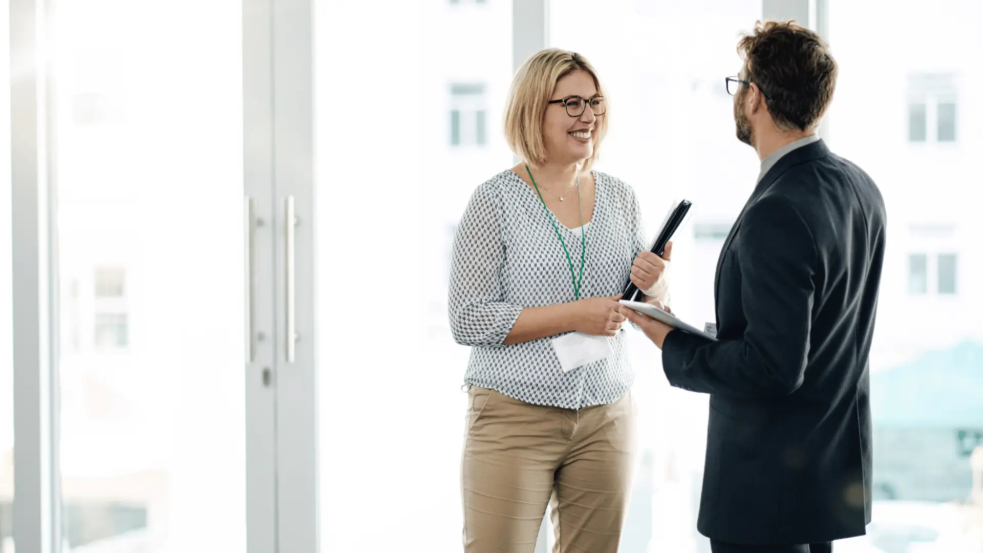 Professional woman with clipboard in trusted advisor conversation with suited colleague