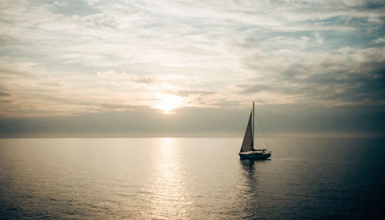A sailboat gliding toward a golden sunrise on calm water — a metaphor for direction and purpose